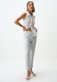 Lichte witte mouwloze blouse met een kraag, gecombineerd met lichtgrijze op maat gemaakte broeken met een trekkoord in de taille en zijzakken.