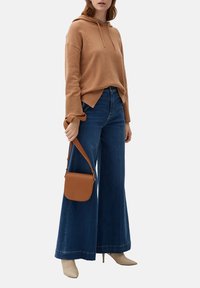 Beige hoodie med ribbade detaljer, kombinerad med vida mörkblå jeans. En solbrun crossbody-väska och beiga högklackade skor fulländar looken.