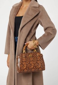 Brun håndtaske med slangeskindseffekt, guld-tone lås og bambus-stil håndtag, kombineret med en beige fluffy frakke. Dekorativ kædearmbånd er synligt.