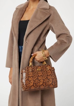 Bolso marrón con efecto de piel de serpiente, cierre de tono dorado y asas estilo bambú, combinado con un abrigo beige peludo. Pulsera decorativa de cadena visible.