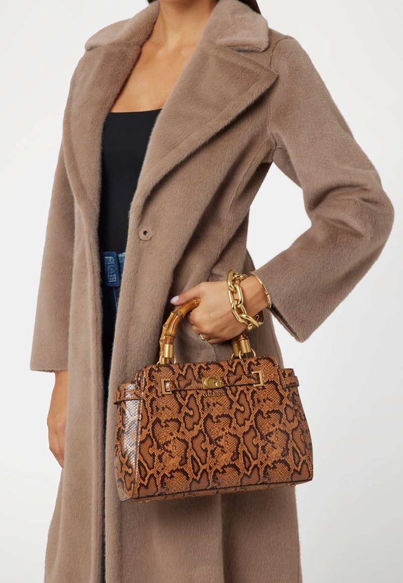 Brun håndtaske med slangeskindseffekt, guld-tone lås og bambus-stil håndtag, kombineret med en beige fluffy frakke. Dekorativ kædearmbånd er synligt.