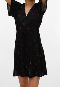 Schwarzes Kleid mit kurzen Ärmeln, V-Ausschnitt, Knopfleiste und einem Bindegürtel. Durchzogen von roten Kirschen und grünen Blättern.