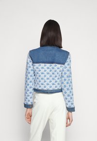 Jeansjacka med ett blått och vitt mönstrat tyg, med en kontrasterande denimrygg och manschetter, lätt kort längd och knapppynt.