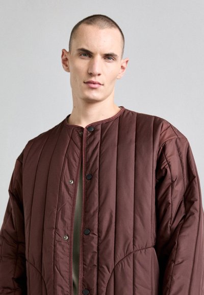 Maroon quilted jacket with a round neckline, snap buttons, and vertical stitching. Soft texture, lightweight design, and relaxed fit.
