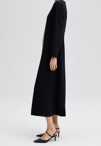 Abito nero a maniche lunghe con vestibilità morbida, caratterizzato da una striscia rosa a contrasto lungo il lato. Abbinato a tacchi slingback neri.