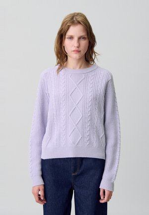 Maglione lavorato a maglia di colore viola chiaro con motivi a diamantini e trecce, scollo rotondo e polsini a coste, abbinato a denim scuro.