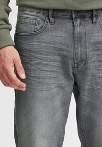 Pelēkas krāsas dženinsu bikses ar vieglu izbalēšanu, priekšējām kabatām un rāvējslēdzēja aizdari. Audums ir gluds ar smalkām svītrām, un bikses ir ar brīvu piegriezumu.