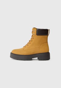 Stivaletti alla caviglia in suede giallo con dettagli marroni, design con lacci, punta rotonda, suola nera spessa e linguetta sul retro per una facile calzata.