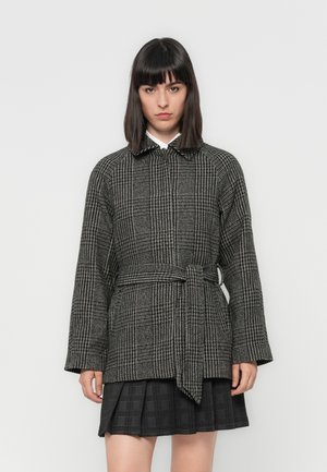 Čierno-biela houndstooth kabát s páskom, ktorý má golier a dlhé, široké rukávy. Skombinované s čiernymi plisovanými sukňami.