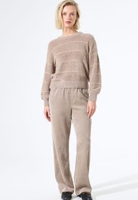 Hellbeige gestrickter Pullover mit feinen horizontalen Streifen, kombiniert mit weichen, hellgrauen Cordhosen. Das Outfit zeichnet sich durch einen bequemen Schnitt und eine angenehme Textur aus.