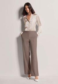 Satin beige blouse met kraag en knoopdetails, gecombineerd met hoge taille, wijde taupebroek en witte puntige hakken.