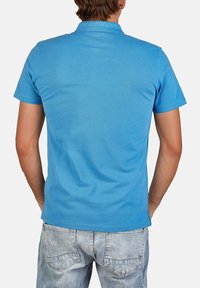 Polo shirt blu in cotone, con colletto classico e maniche corte, abbinato a jeans in denim chiaro. Texture liscia, vestibilità casual.