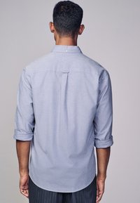Hellsblaue Button-Down-Hemd mit hochgekrempelten Ärmeln, Rückenfalte und abgerundetem Saum. Hergestellt aus einem strukturierten Stoff.