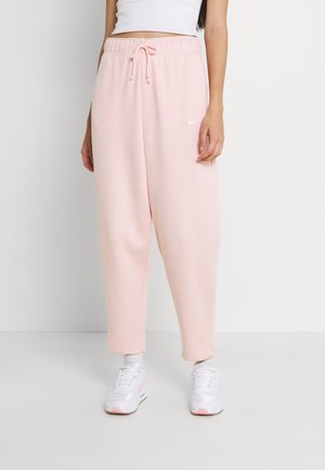 Vrouw draagt lichtroze Nike sweatpants met een trekkoord in de taille, witte sokken, witte sneakers en een cropped wit topje.