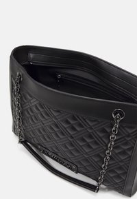 Czarna pikowana skórzana torebka z łańcuchowymi ramiączkami, otwarta u góry, z widoczną wewnętrzną kieszenią na zamek i gładkim skórzanym wykończeniem.