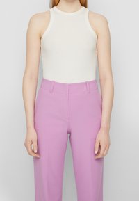 Top halter blanco con textura acanalada y silueta ajustada, combinado con pantalones de talle alto en color lavanda que cuentan con pliegue delantero y bolsillos laterales.