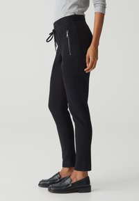 Jogging en suède noir avec une coupe slim, dotés de poches zippées et d'une taille à cordon. Texture lisse et design à longueur de cheville.