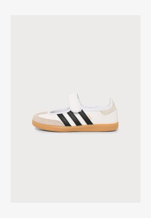Sneaker bianca e beige con strisce nere, suola in gomma e cinturino in velcro, mostrata di lato su sfondo semplice.