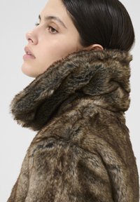 Barna árnyalatú műszőrme kabát, magas gallérral, texturált felülettel és puha kivitelben. A dizájn kényelmes, luxus megjelenést kölcsönöz.