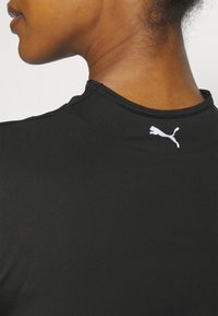Camiseta deportiva negra con cuello alto, con una superficie texturizada y un pequeño logo de Puma en blanco en la parte trasera del cuello.