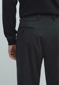Černé kalhoty s hladkou texturou látky, štíhlým střihem a zadní kapsou s knoflíkovým detailem.