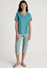 Turquoise V-hals t-shirt van zacht materiaal, gecombineerd met gestreepte capri-broek met een bloemmotief in blauwe, roze en groene kleuren.