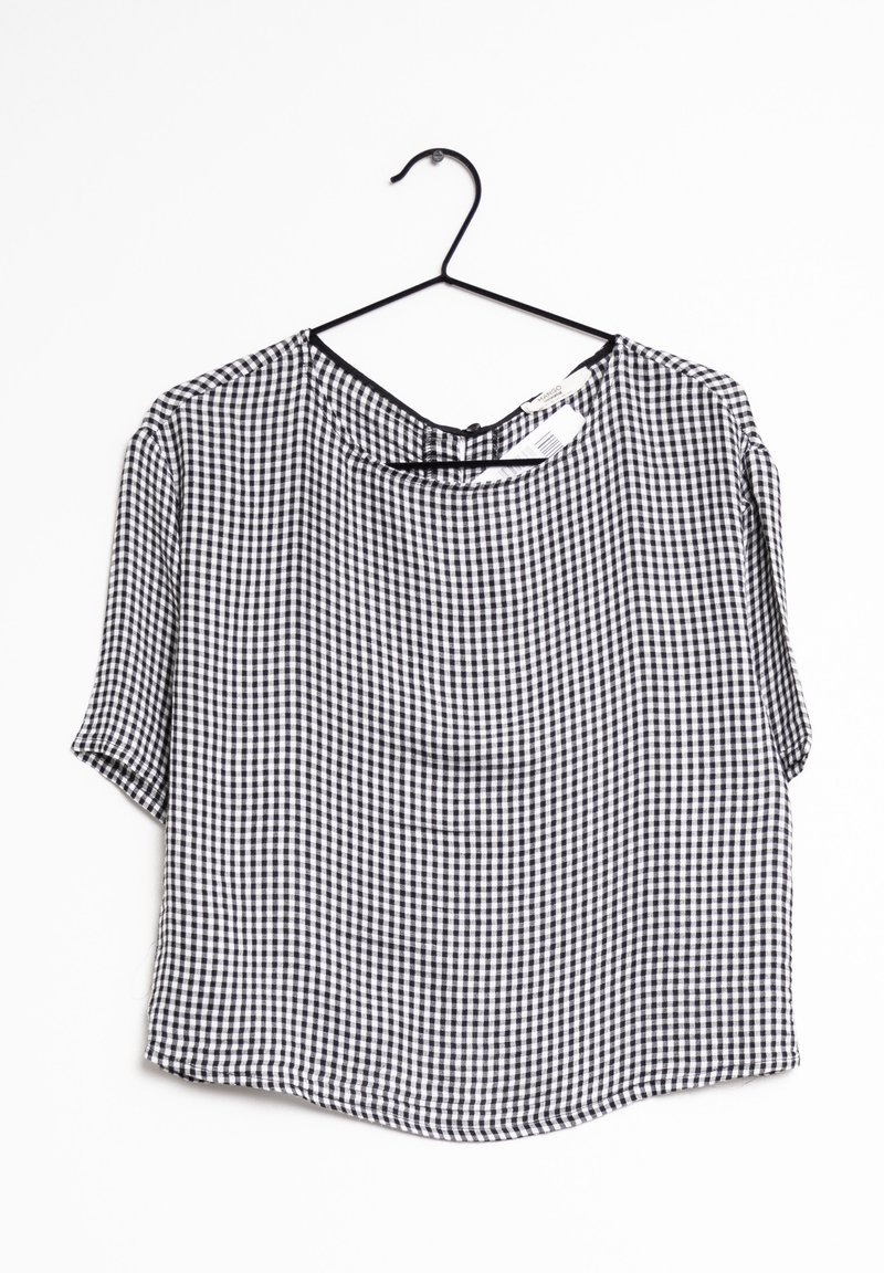 Blouse manches courtes à carreaux noirs et blancs sur un cintre. Dotée d'un col rond et d'un ourlet légèrement arrondi. Tissu léger.