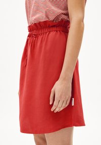 Falda roja hasta la rodilla con cintura elástica y cordón. Textura suave, etiqueta lateral, combinada con una blusa a rayas.