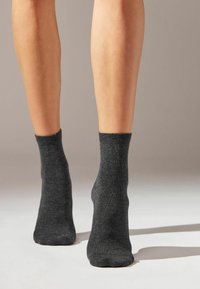 Graue Knöchelsocken aus einem strukturierten Stoff, eng am Knöchel anliegend, mit einer glatten Oberfläche und einem dezenten gerippten Bund.
