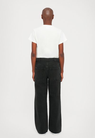 Jeans amplios negros y una camiseta blanca lisa, vistos desde atrás. Los jeans tienen dos bolsillos traseros y un ligero desgastado en el color.