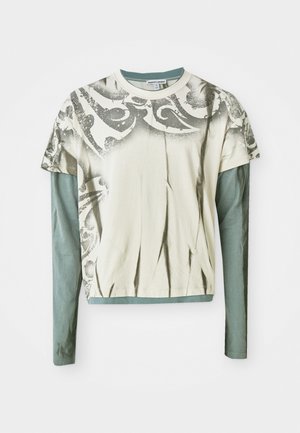 T-shirt gráfico de manga longa com um corpo creme e uma estampa cinza decorativa, e uma camada inferior de manga longa em teal. Textura de tecido suave.