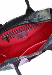 Öppen tote-väska med mörkblå denimutsida, klart röd tyginsida, inre ficka med dragkedja och svarta handtag.