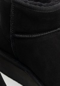 Czarny zamszowy botek za kostkę z miękką wyściółką wewnętrzną, kontrastującym przeszyciem i płaską gumową podeszwą; minimalny design bez widocznych wzorów.