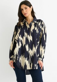 Long-sleeve blouse in navy and cream with an abstract pattern, collared neckline, and a curved hem. Smooth, lightweight fabric.