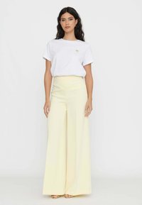 T-shirt bianca con un piccolo accento dorato, abbinata a pantaloni ampi giallo limone a vita alta, che mostrano una trama e una caduta morbida.