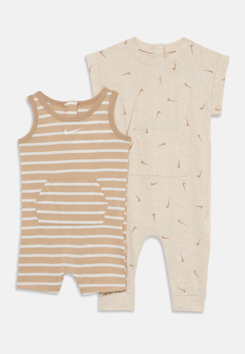 El conjunto de dos piezas incluye un mono de tirantes a rayas marrón y blanco con un bolsillo frontal, y una camiseta corta beige con un patrón del logo de Nike.