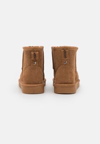Brune semskede ankelstøvler med rund tå, flad sål og elastiske sideaccentuer. Har et syet design og mærkeklistermærker.