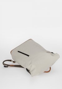 Zaino in tessuto beige con dettagli in pelle marrone, forma rettangolare, spallacci regolabili e una tasca con zip su un lato.