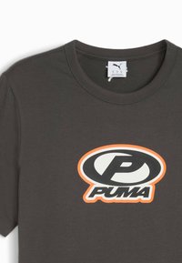 Grå bomulds-t-shirt med et stort, cirkulært sort-hvidt logo med en orange kant, der har "PUMA" i midten. Korte ærmer.