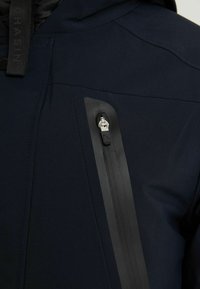 Granatowa ocieplana kurtka z fakturowanym wierzchem, kieszenią na suwak z czarną lamówką oraz stójką.