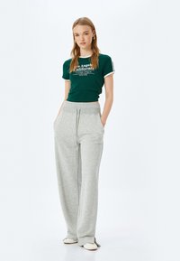 Camiseta verde de corte corto con ribete blanco y texto impreso, combinada con pantalones de chándal grises, holgados, con cintura elástica y bolsillos laterales.