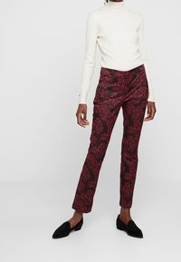 Bílý žebrovaný rolák v kombinaci s burgundskými kalhotami s listovým vzorem, doplněný černými slip-on botami.