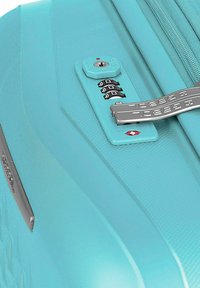 Una valigia rigida turchese con lucchetto a combinazione, superficie texturizzata e zip liscia con accenti in argento.
