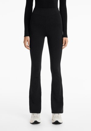 Zwarte flared leggings van glad, elastisch materiaal, met een hoge tailleband en zijzakken. Geaccentueerd met subtiele naden voor een gestroomlijnde uitstraling.