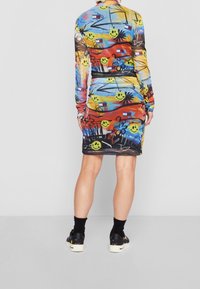 Vestido de manga larga con un estampado gráfico colorido que presenta caritas sonrientes, palmeras y formas abstractas en tonos vibrantes. Silueta ajustada.