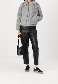 Giacca in pelliccia sintetica grigia con texture a zigzag, maglione grigio a coste, pantaloni in finta pelle nera e sneakers nere con strisce bianche. Borsa nera.