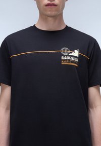 Sort bomulds T-shirt med rund hals, prydet med orange og hvide trykte grafikker, herunder et globus- og bjergdesign på brystet.