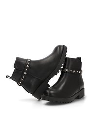 Botas de cuero negras hasta el tobillo con una suela gruesa, que presentan una correa adornada con estrellas alrededor del tobillo y una lengüeta para facilitar su colocación.