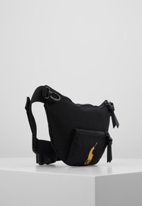 Svart nylon crossbody-väska med justerbart rem, som har en framficka med dragkedja och guld-logodetaljer. Slät textur och kompakt design.