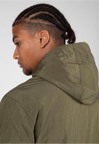 Olivengrüne Kapuzenjacke mit strukturiertem, leichtem Stoff. Details an den Nähten und eine lässige Passform mit langer Kapuze.